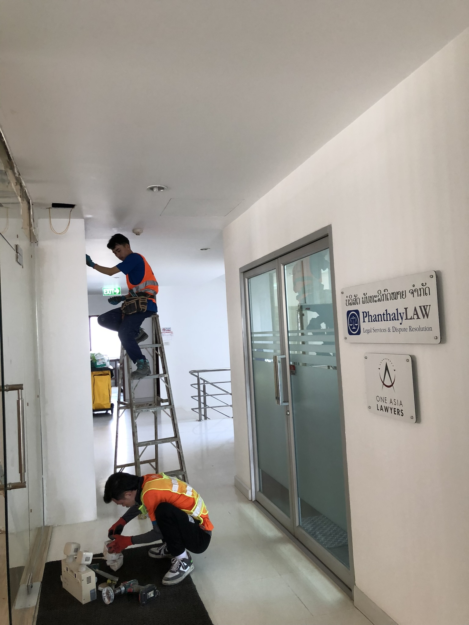 ຊ່າງກຳລັງເຮັດວຽກຂະຫຍາຍລະບົບແຈ້ງເຕືອນໄຟໄໝ້ໃນທາງເດີນສຳນັກງານ